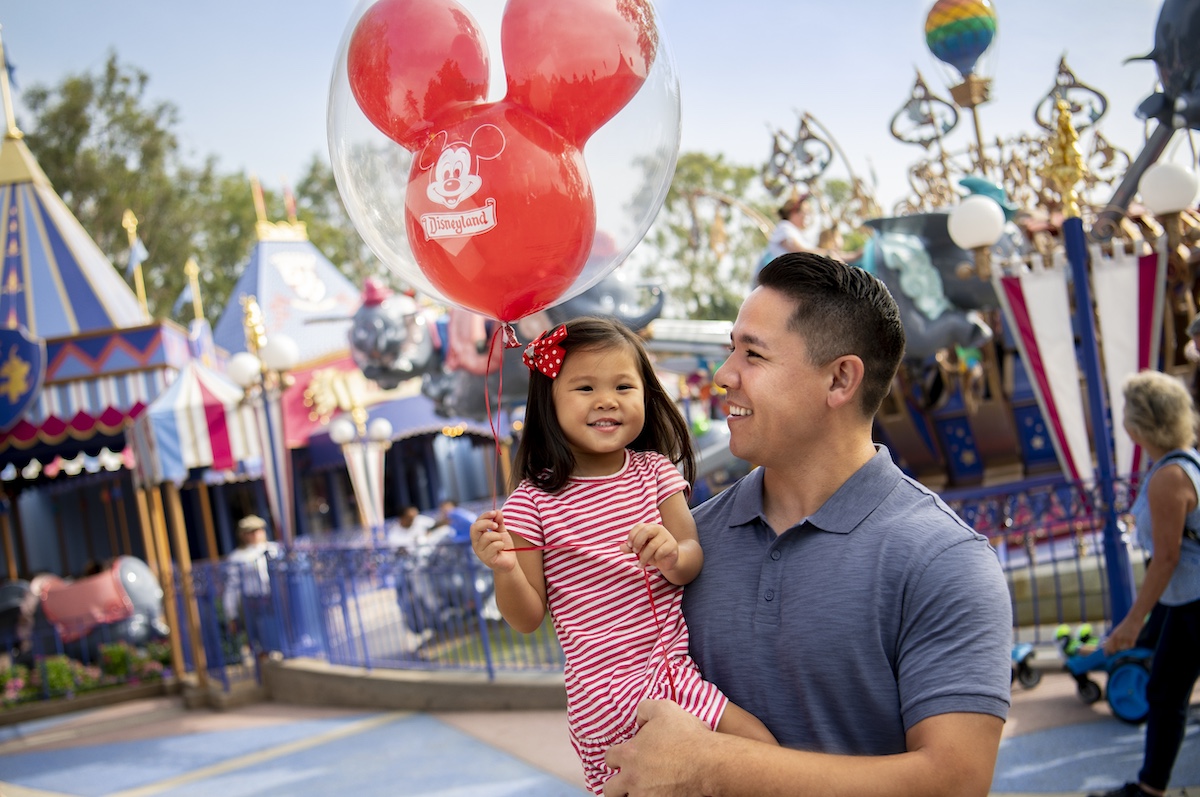 man and child standing in fantasyland at disneyland resort holding mickey balloon
