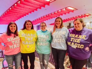 Share the Magic Travel agents posing in matching Share the Magic sweaters that are in multiple colosr